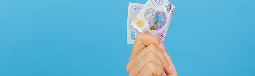 Isolated hand holding £20 (20 pounds sterling) against blue background