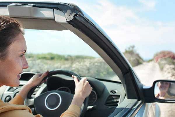 Young woman driving convertible car on sunny day down dirt track. Point of view over shoulder