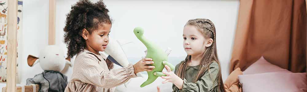 Two little girls sitting on bunk bed sharing toy green dinosaur