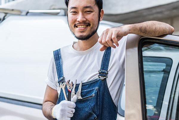 Young asian man holding tools whilst leaning on a van door. He insured the van with temporary van insurance.