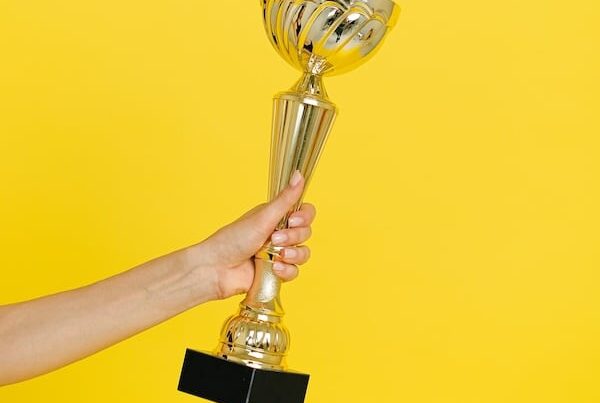hand holding a trophy in front of a yellow background