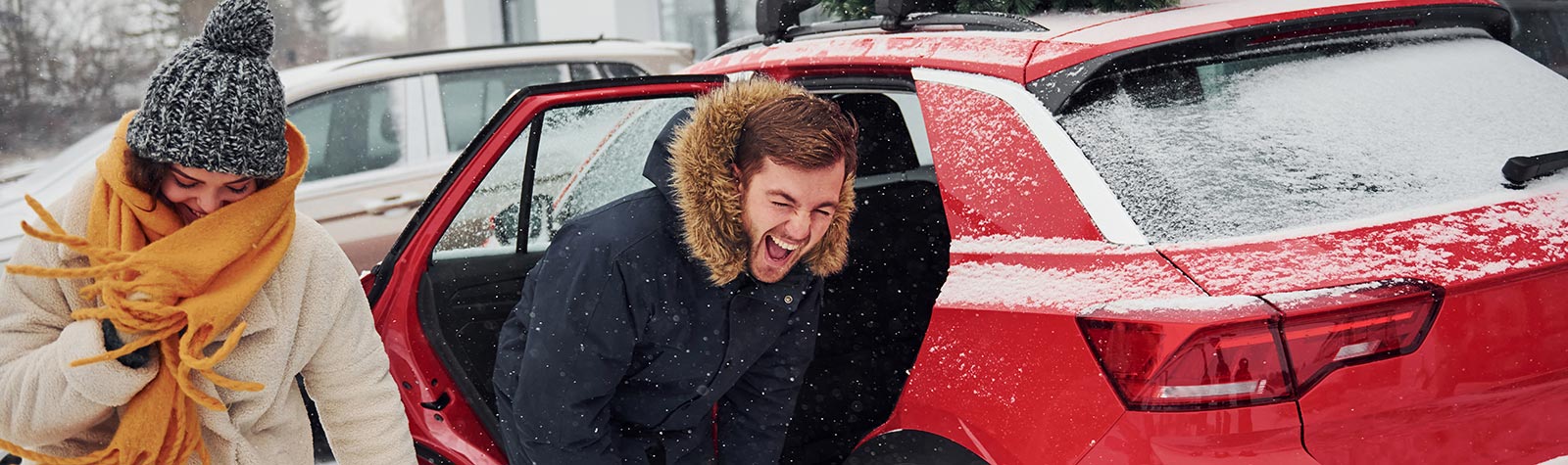 Young couple laugh beside snow covered car
