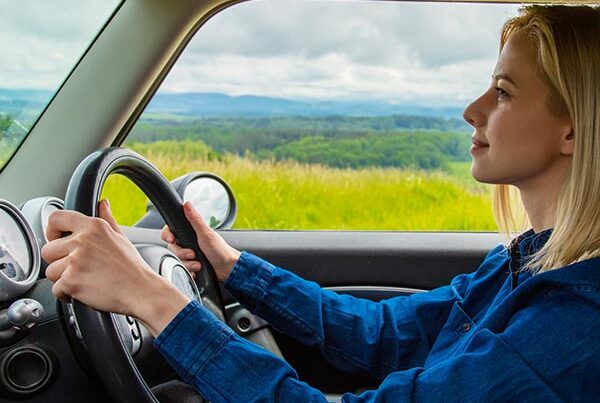 Blonde woman driving a car with background hills