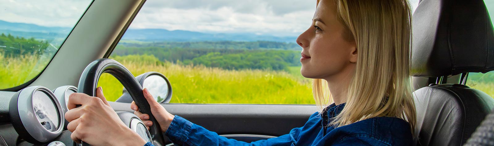 Blonde woman driving a car with background hills
