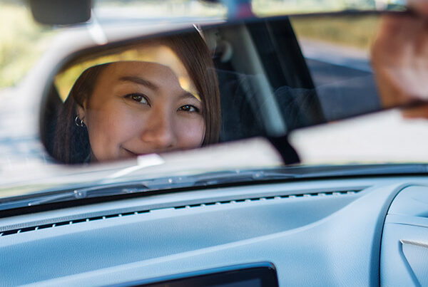 Smiling young female driver adjusting rear view mirror. She is pleased she has used zixty to insure a learner