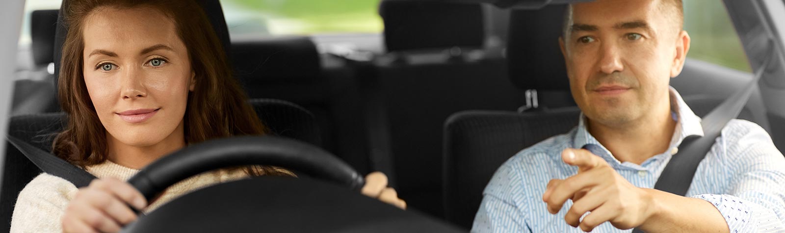 Man supervising a female learner driver at the wheel of a car.